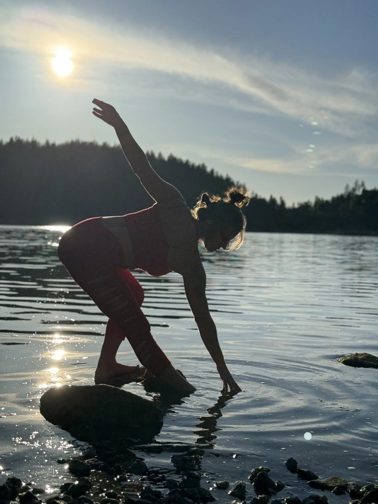 Person practicing yoga on rocks by a lake at sunset