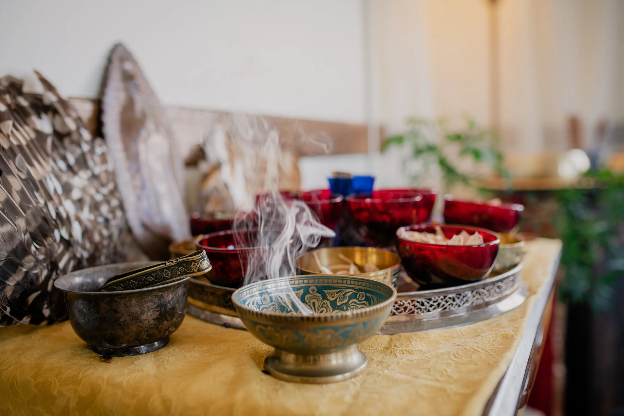 Various steaming bowls and dishes on a yellow tablecloth, with a blurred background of a room with plants and sunlight.