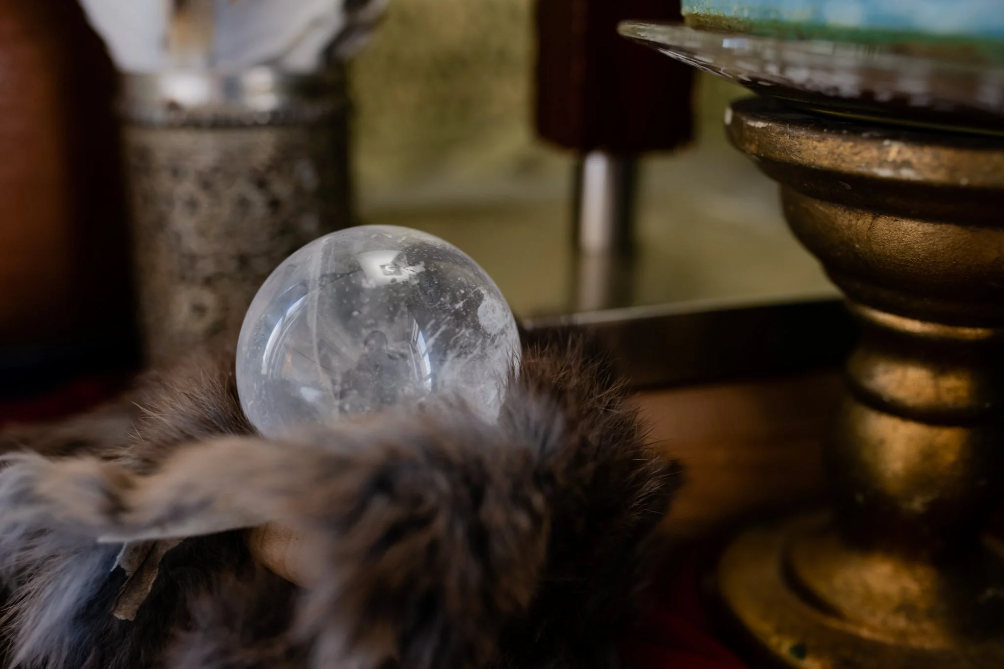Close-up of a ball of clear glass with water droplets, surrounded by various objects and a fur print at the bottom edge.