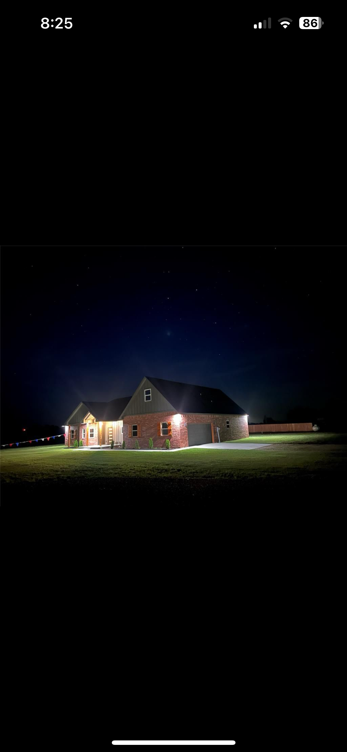 A house with exterior lights on, situated on a well-maintained lawn at night, with a clear starry sky overhead.