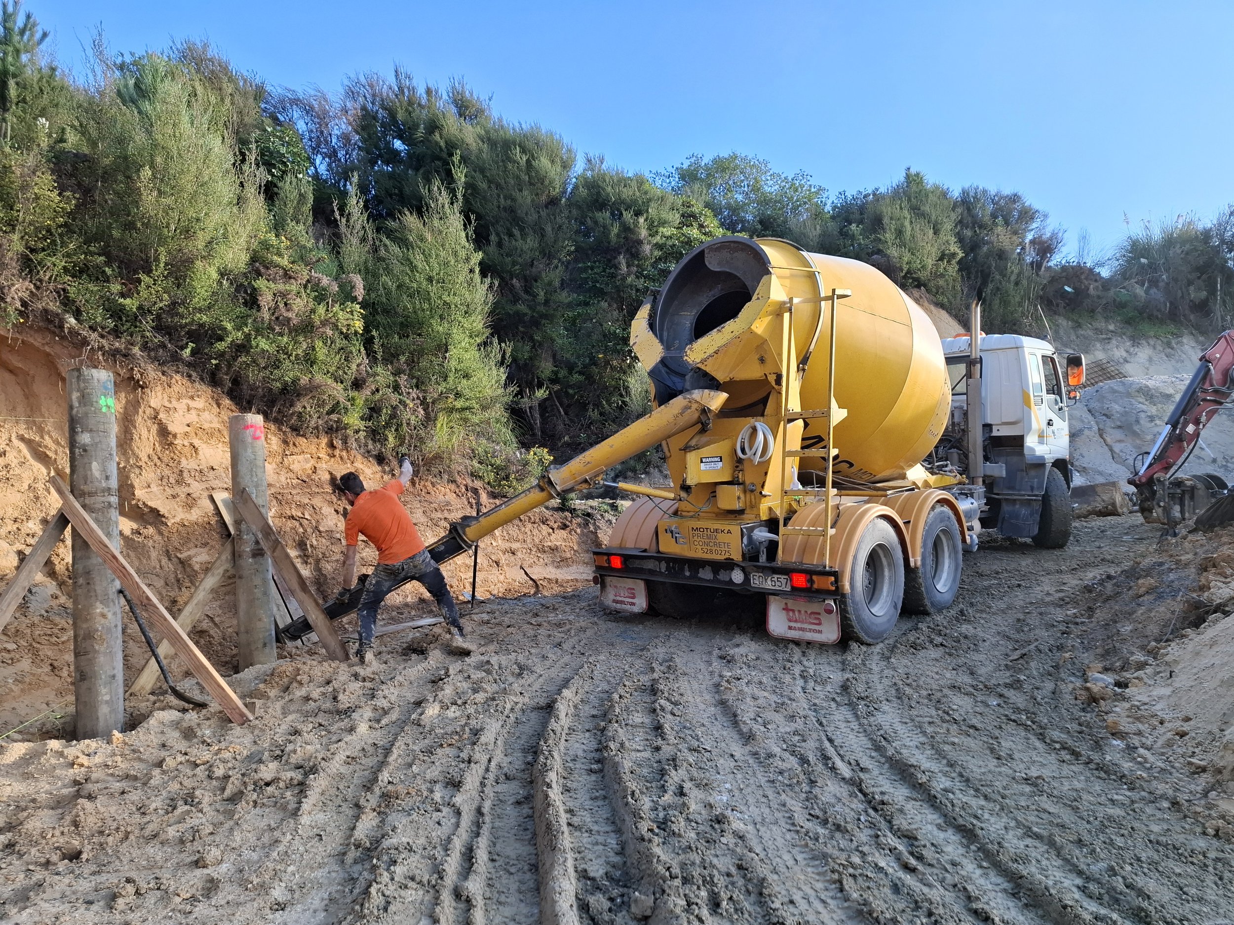 Construction workers and a cement mixer truck working on a hillside with plants and clear blue sky.