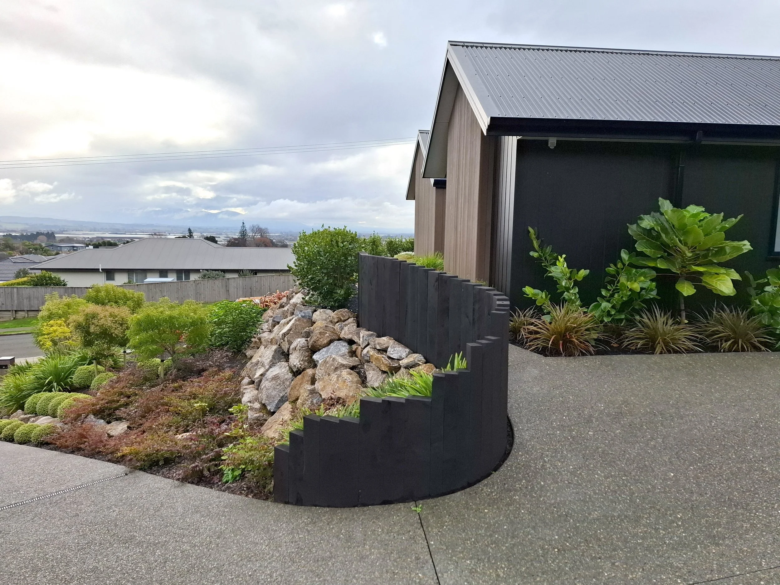 A residential neighborhood with modern houses, landscaped gardens, and a scenic view of distant mountains under cloudy skies.