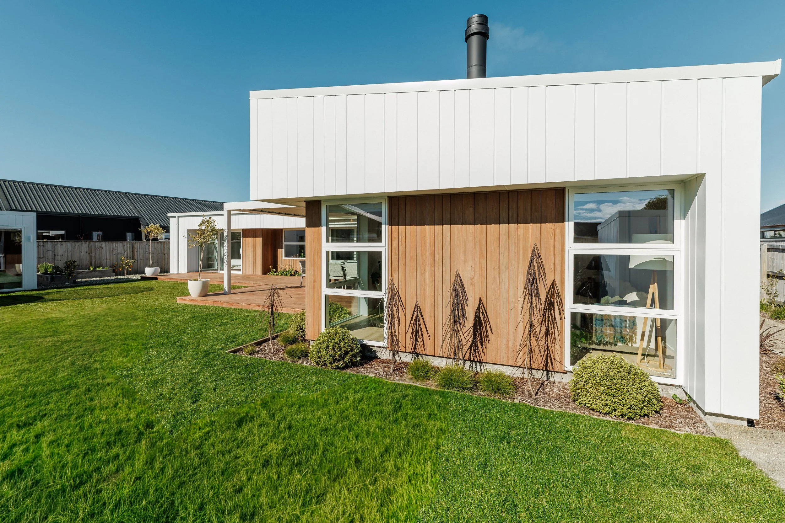 Modern house with wood and white exterior, large windows, green lawn, and a clear blue sky.