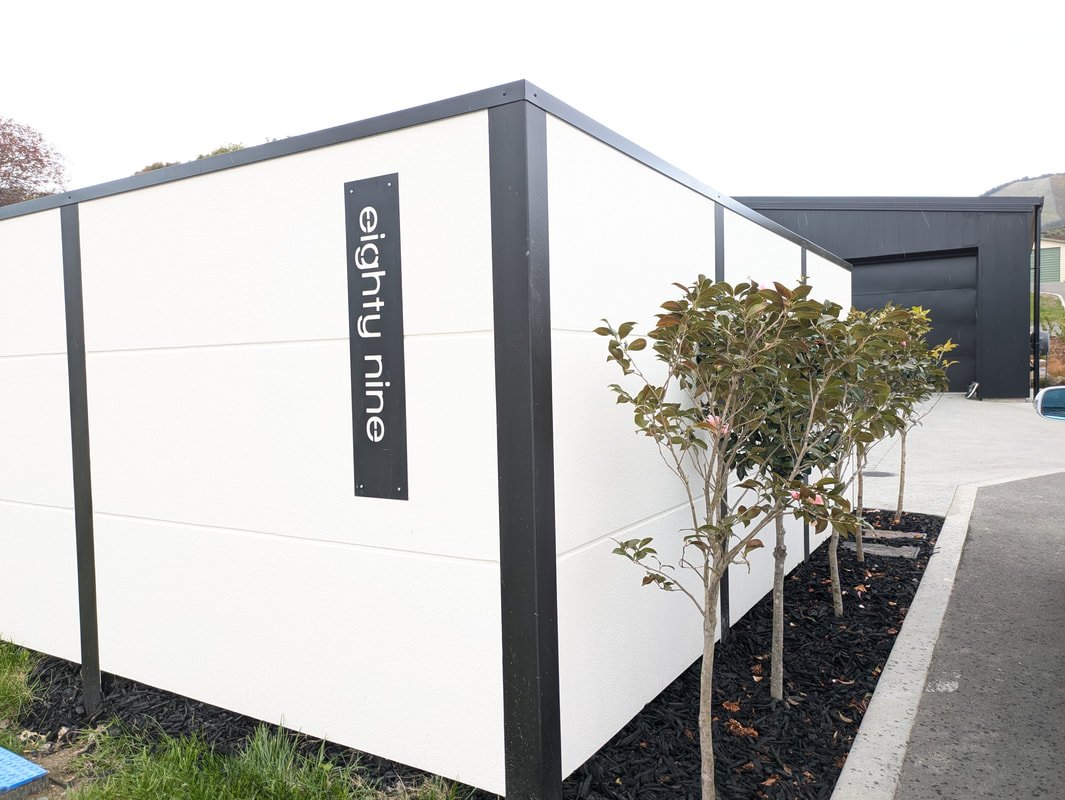 Modern building with black and white exterior walls, small trees planted along the sidewalk, and a sign that reads "elighty nine".
