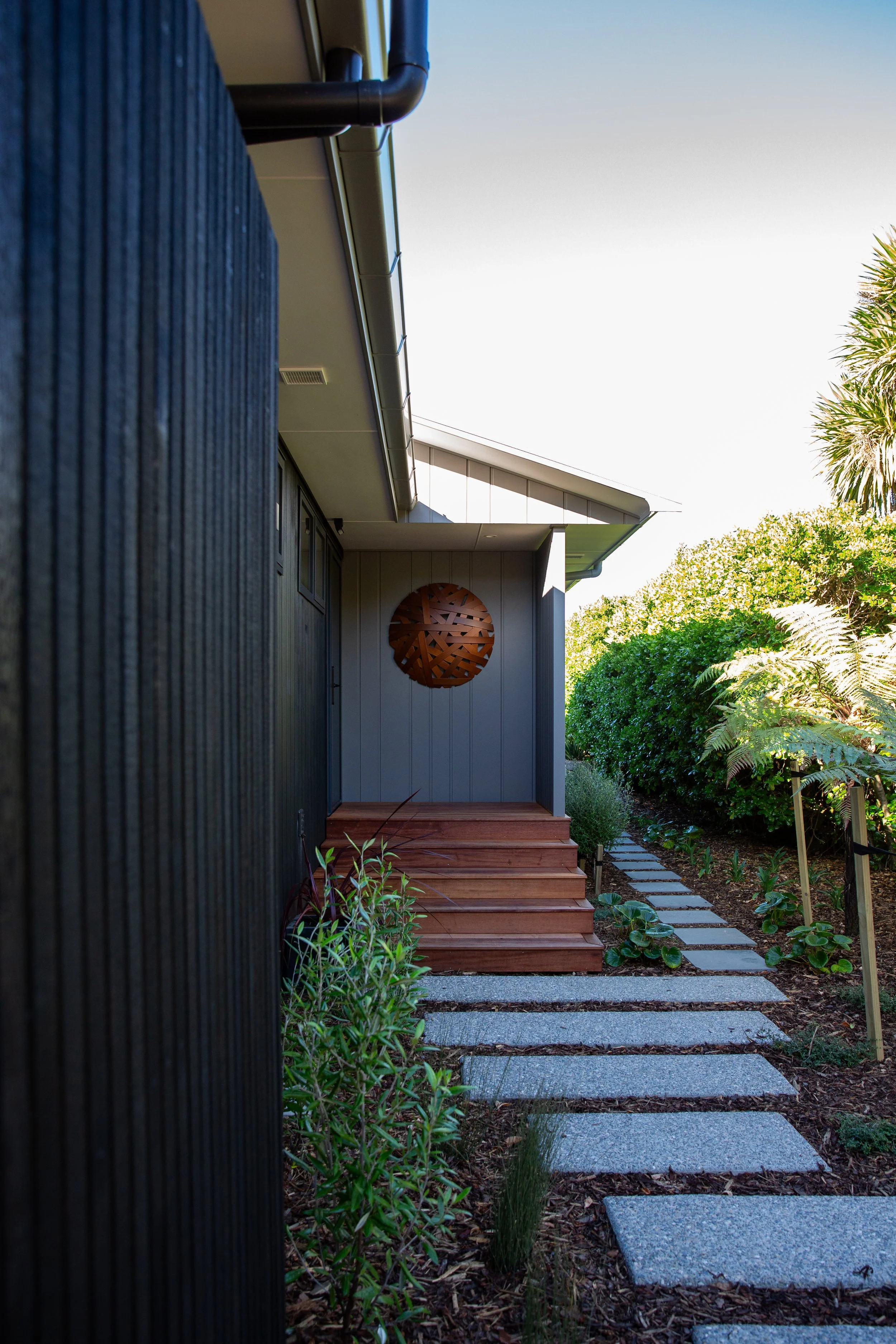 Ruby Bay Renovation featuring native and coastal NZ planting. Custom concrete stepping pavers. Pathway up to the front door including kwilia steps.