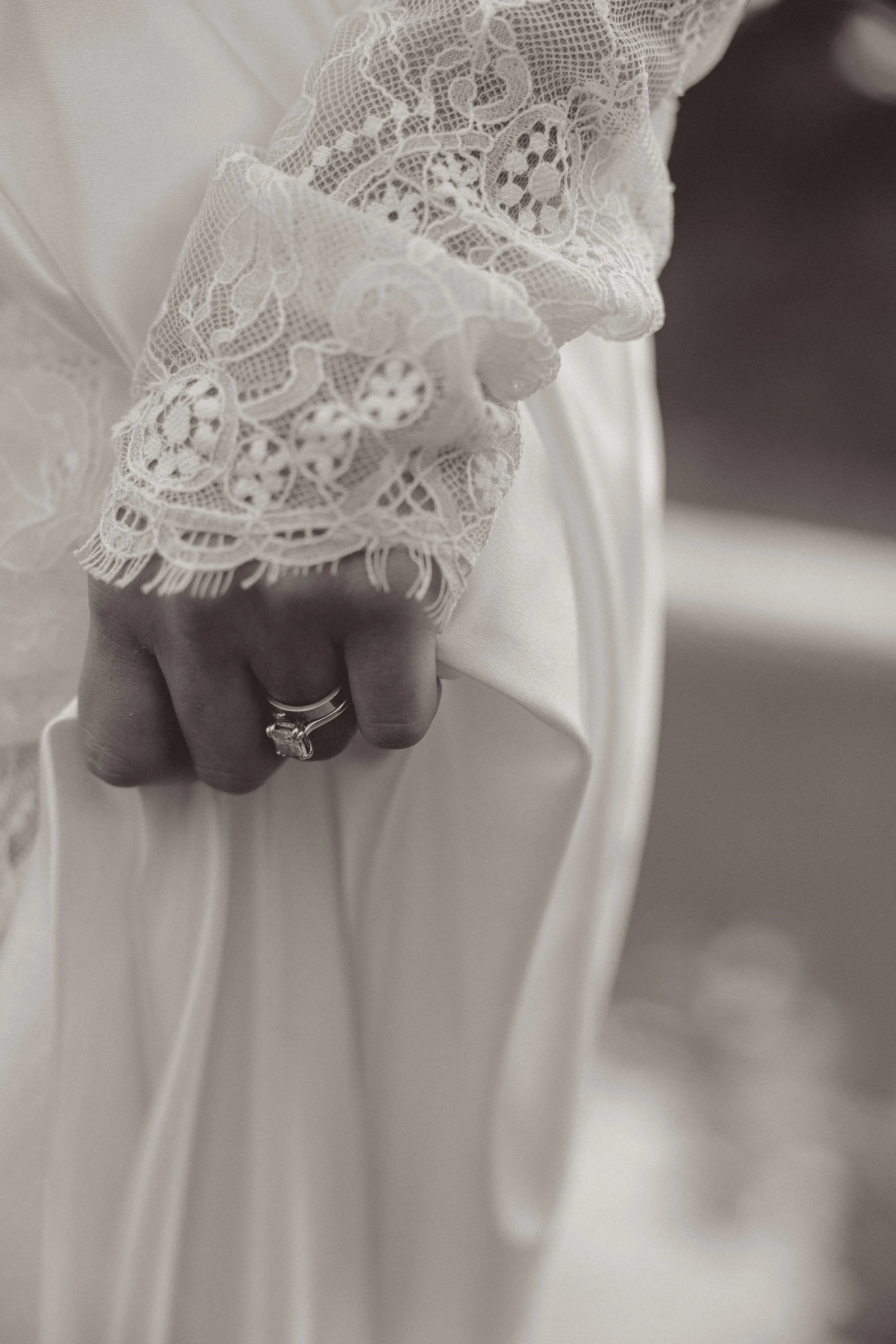 Close-up of a woman's hand with an engagement ring, dressed in lace sleeve, holding a satin dress.