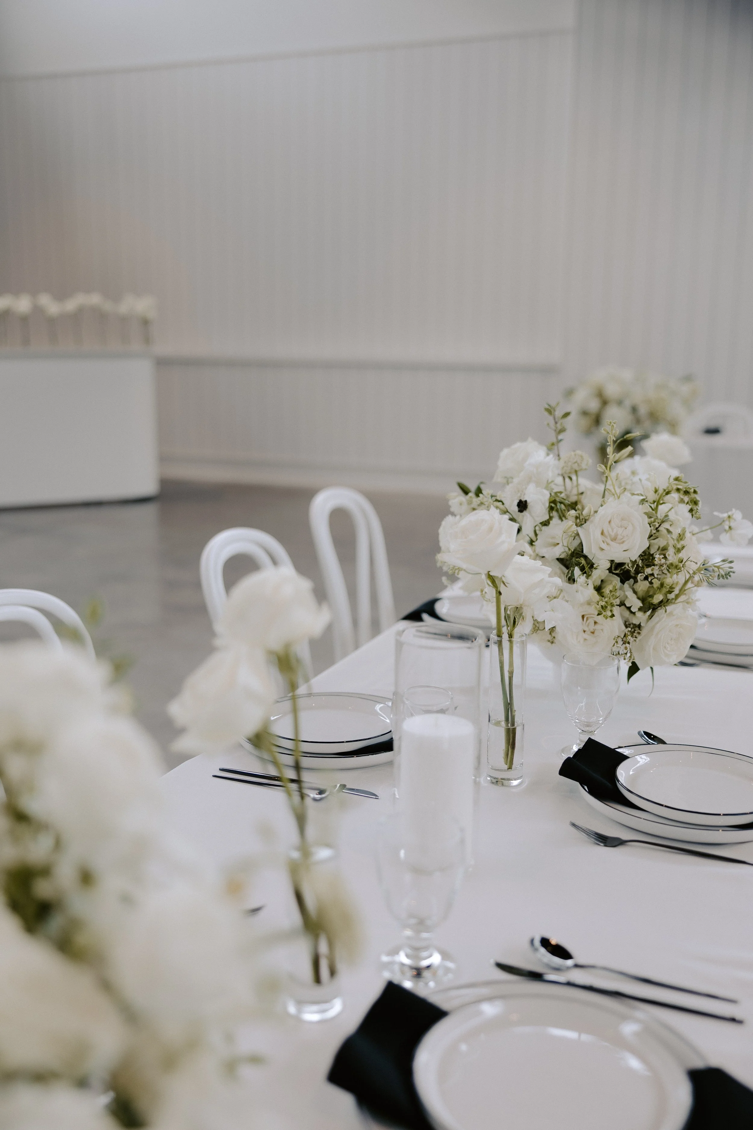 Elegant dining table setup with white floral centerpieces, plates, glasses, and black napkins.