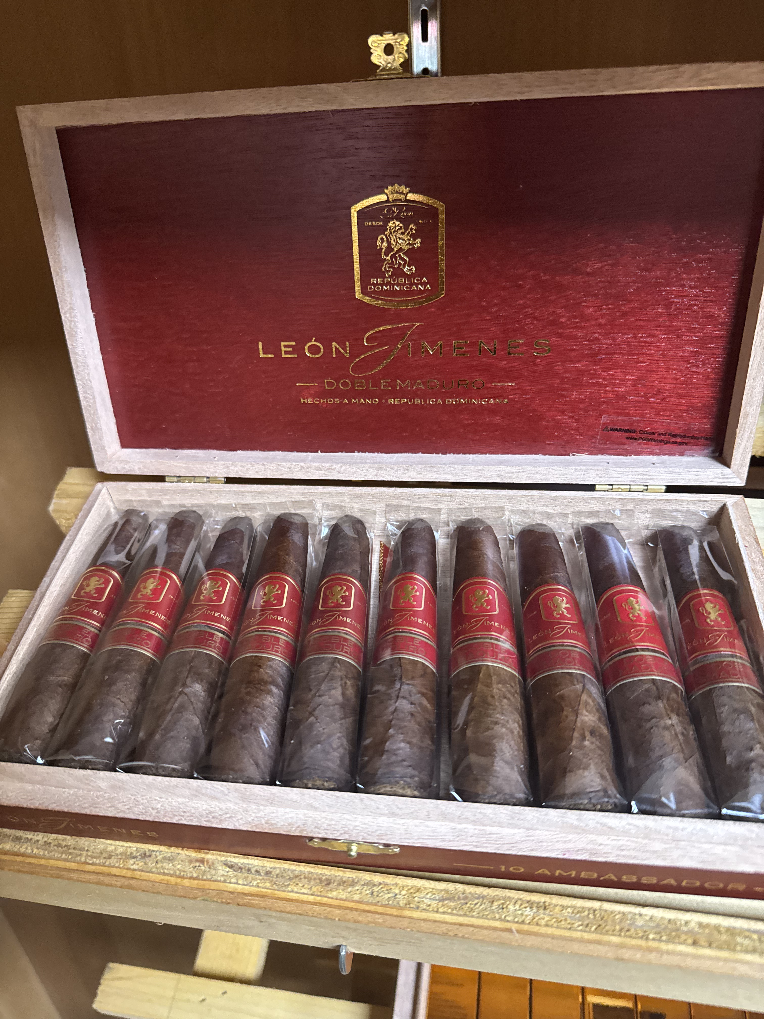 A wooden box of León Jimenes cigars, showing ten cigars with red and gold labels inside the box.