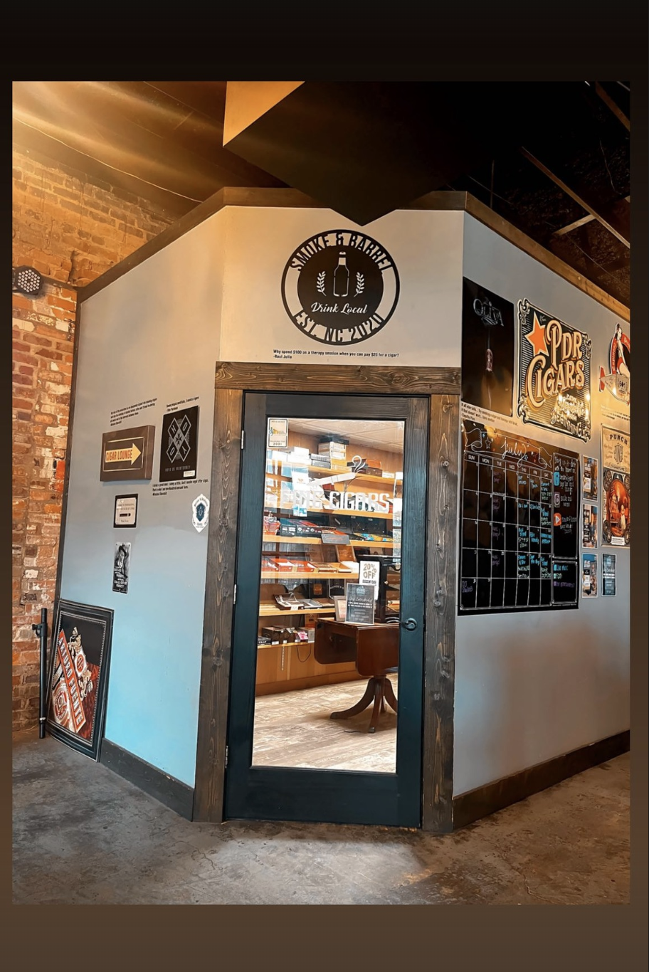 Interior view of a cigar shop or lounge with a glass door, cigar-related signs, and a wall calendar.
