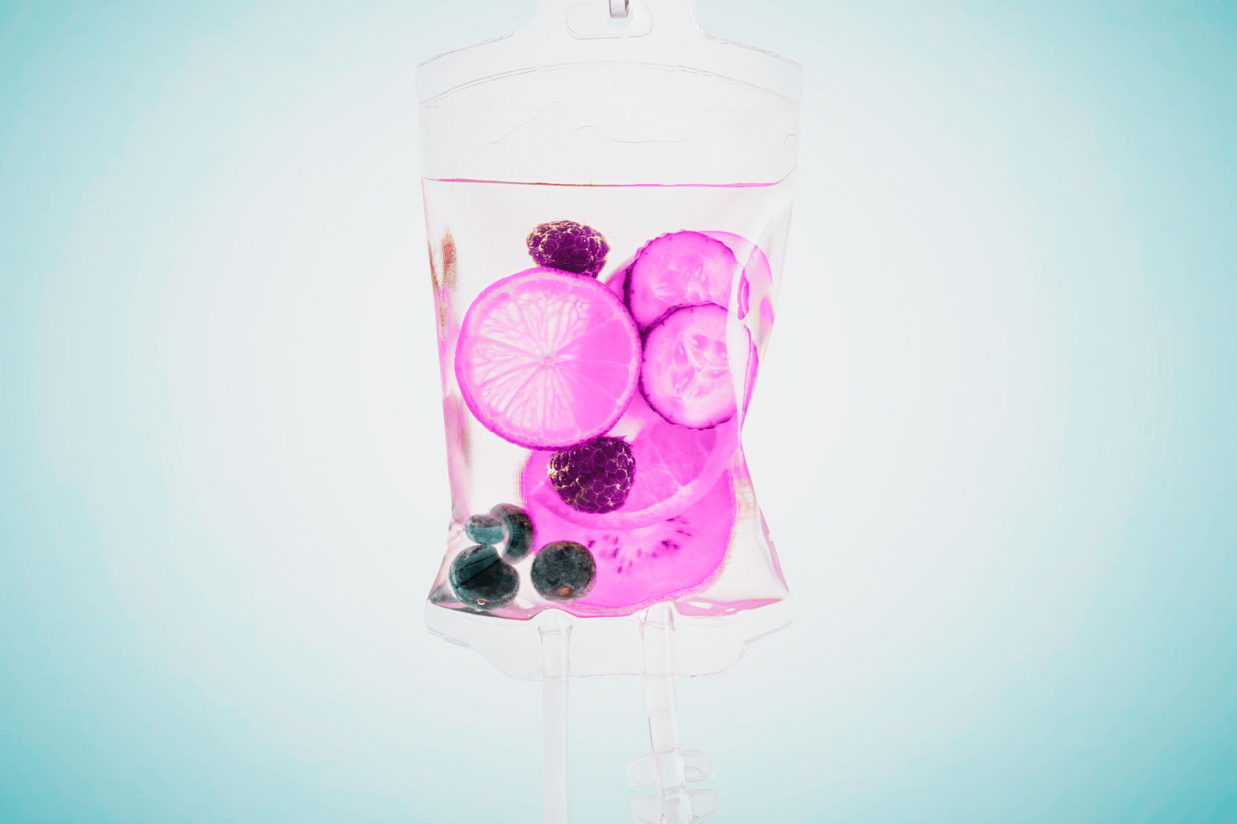 A cleaved lemon, cucumber, blackberry, blueberry, and kiwi slices in a clear IV drip bag filled with water.