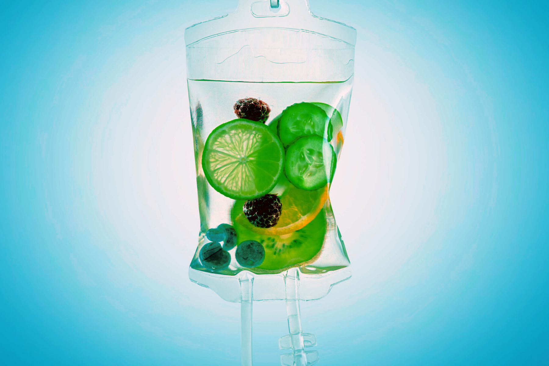 A clear IV bag filled with slices of lime, cucumber, blueberries, and blackberries, with a light blue background.
