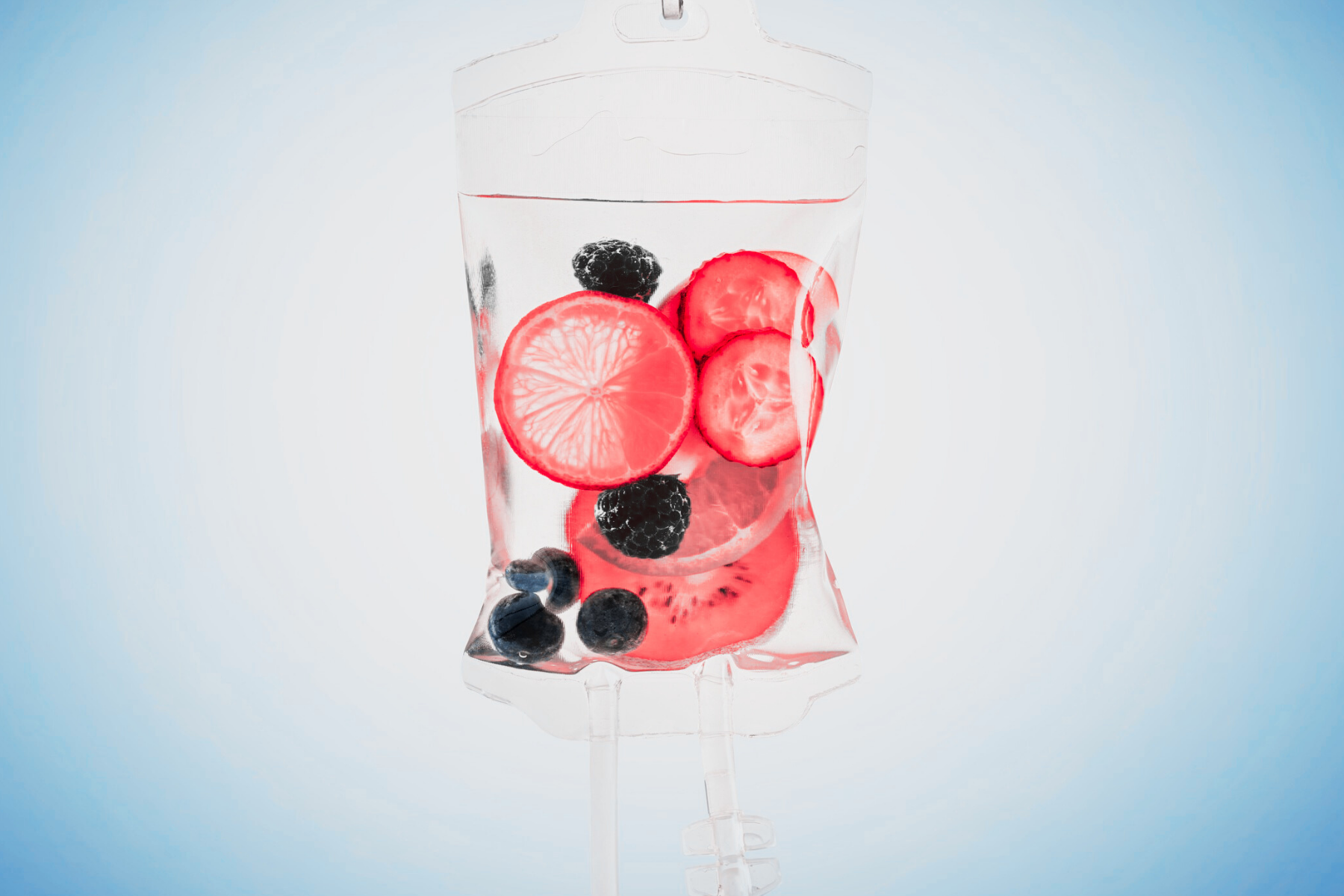 A clear intravenous drip bag filled with slices of lemon, tomato, cucumber, blackberries, blueberries, and raspberries.