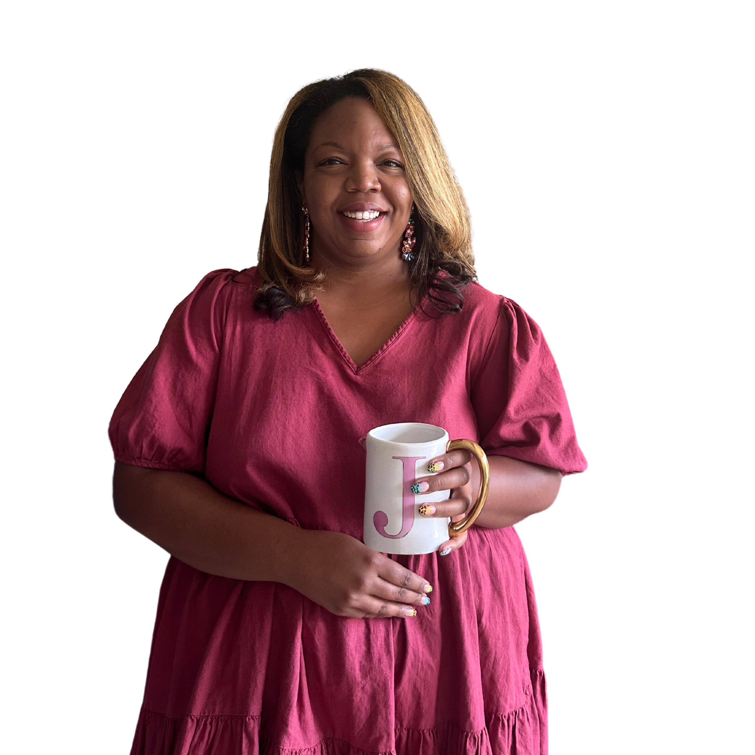 A woman smiling and holding a white mug with a pink letter 'J' on it. She is wearing a pink dress and has colorful nail polish.