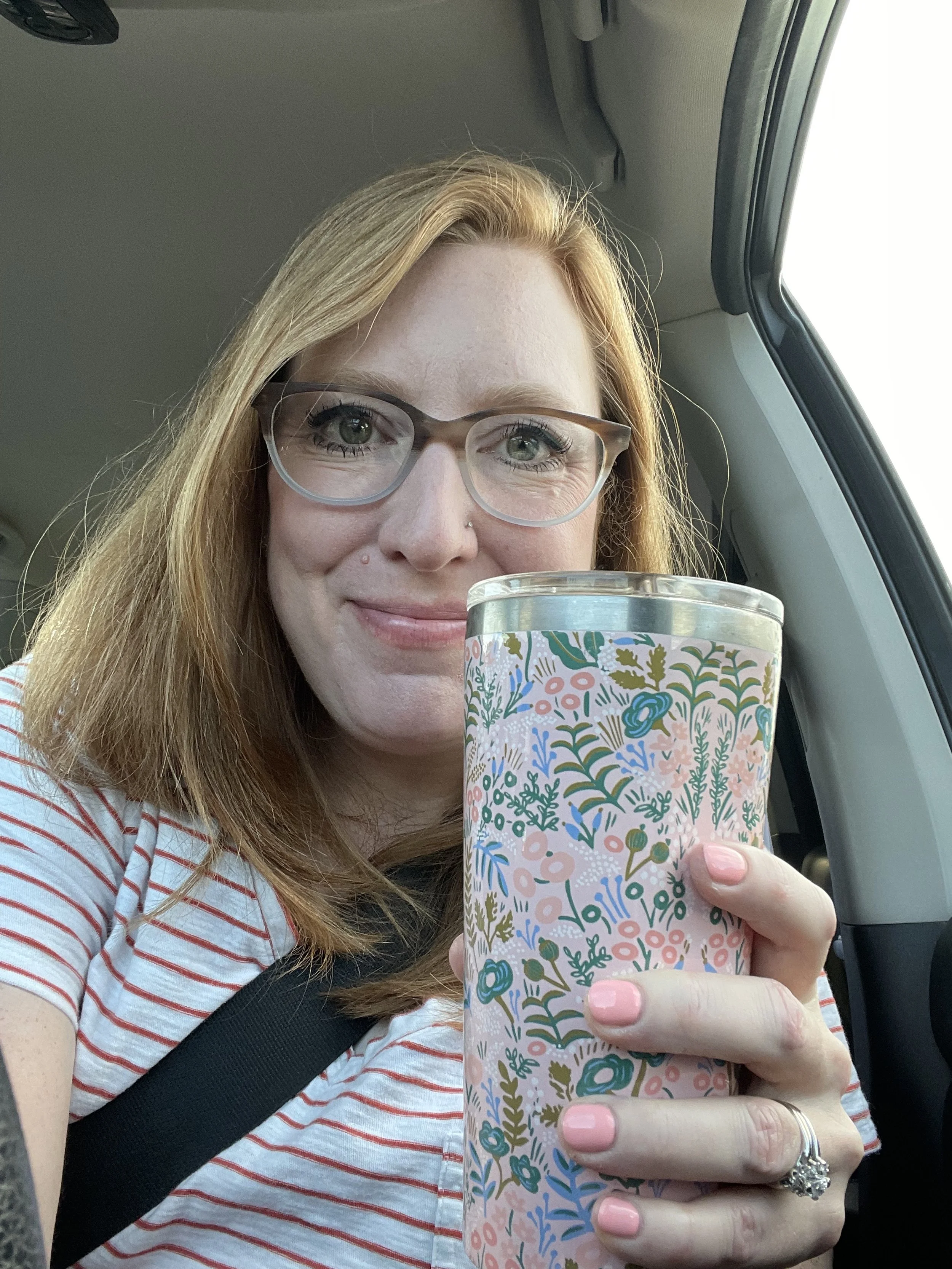 A hand holding a white cup of latte with latte art, while milk is being poured into the coffee.
