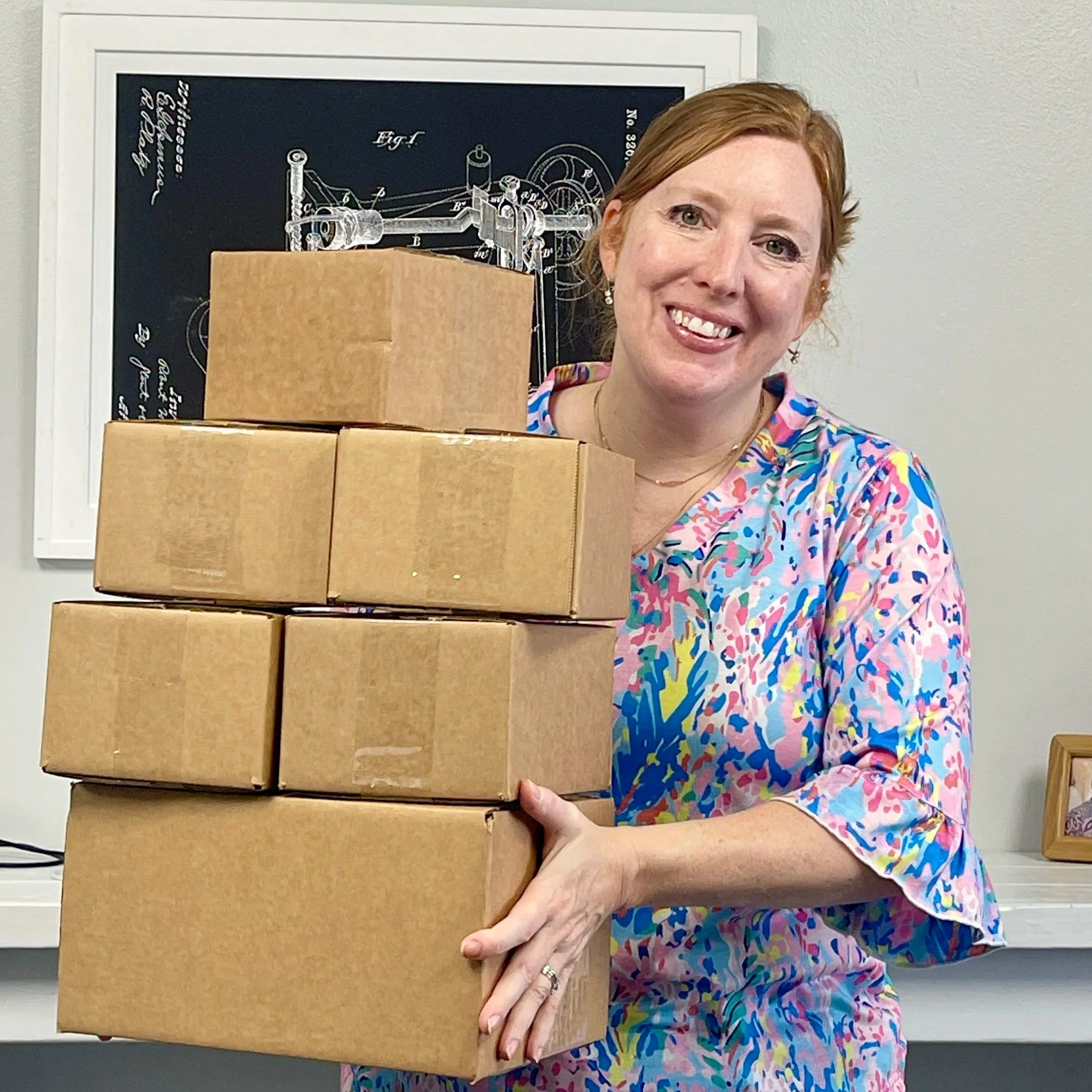 A flat lay of a white keyboard with a gold heart-shaped clock, pink and white flowers, candles, gold dollar signs, a ring, and a pink macaron on a white and pink background with a gift box.