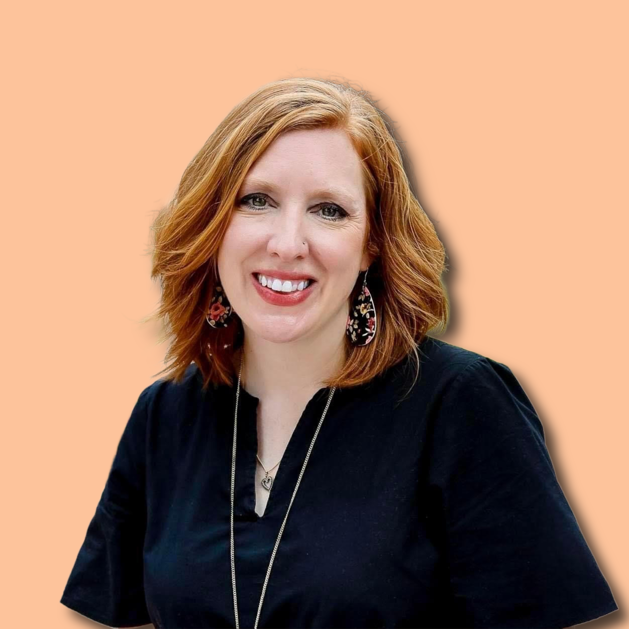 A woman with red hair smiling, wearing earrings, a necklace, and a black shirt, against a peach background.