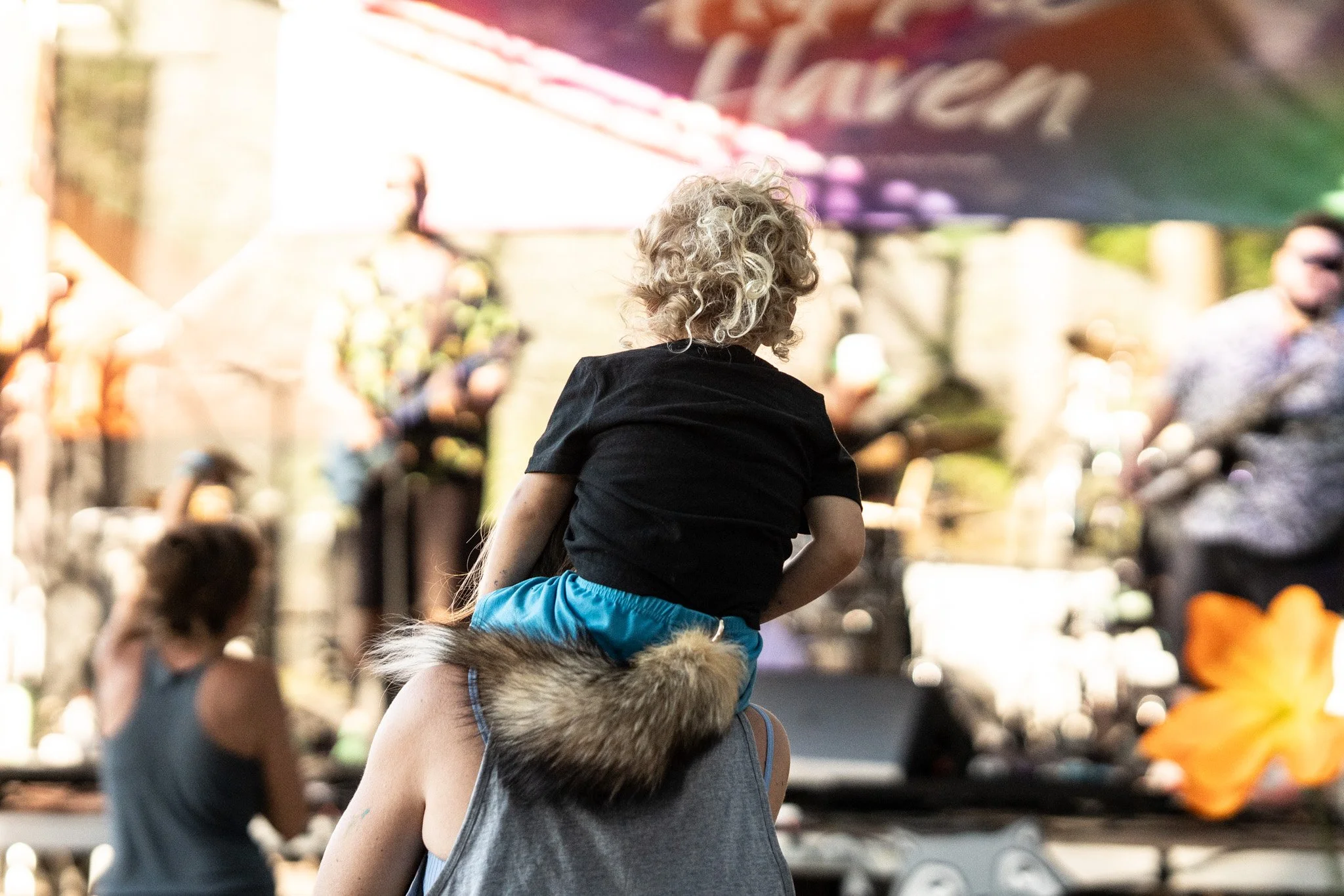 A child with a foxtail rides on his fathers shoulders