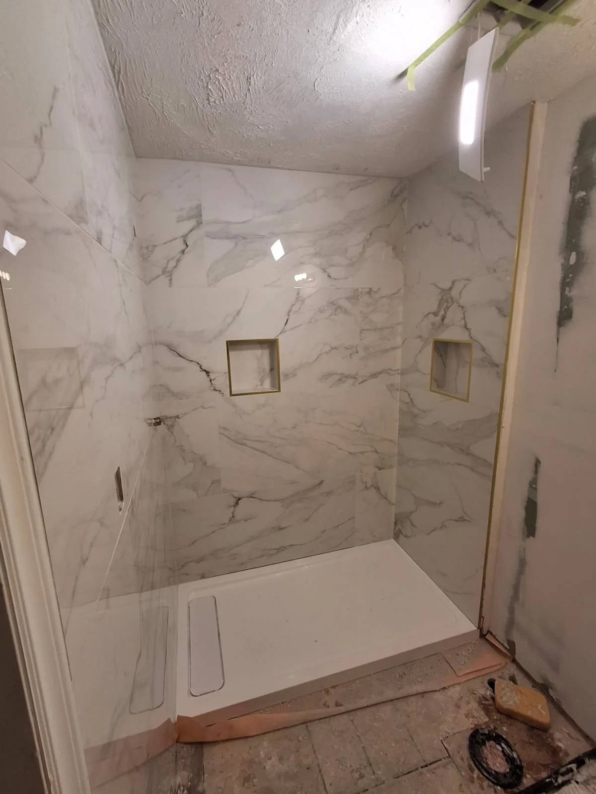 A modern shower with marble walls, two square recessed shelves, and a white shower base.
