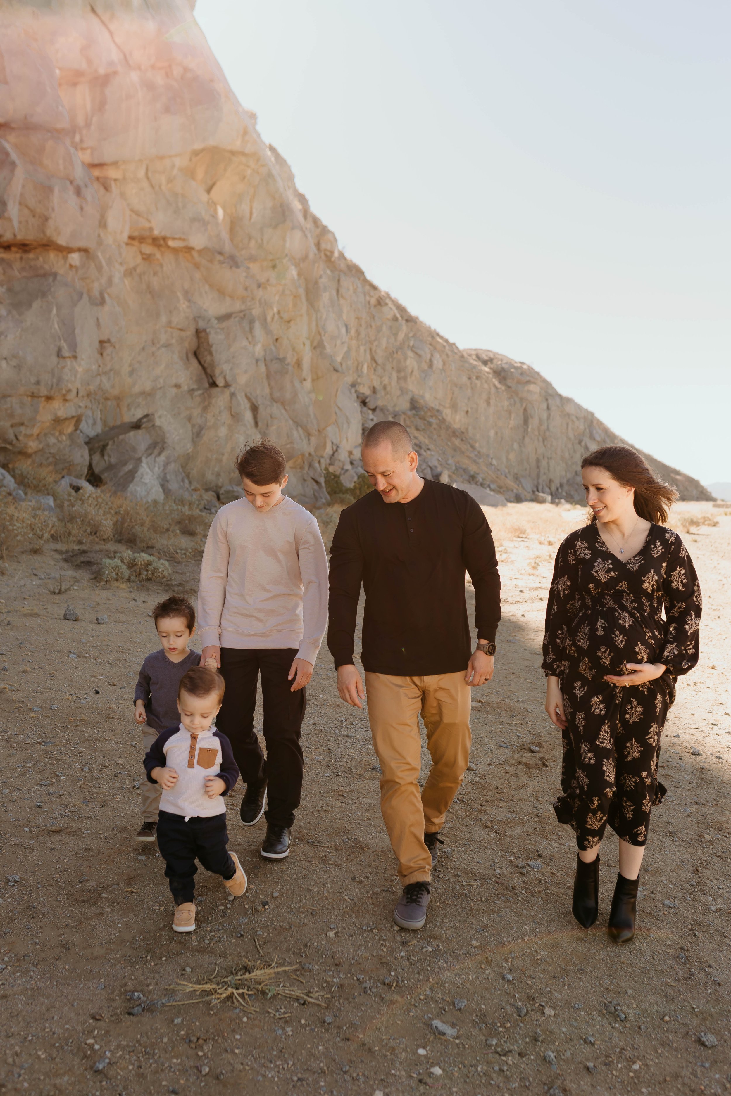 A bride and groom kiss during outdoor wedding ceremony with guests in background, green trees, house, and blue sky.