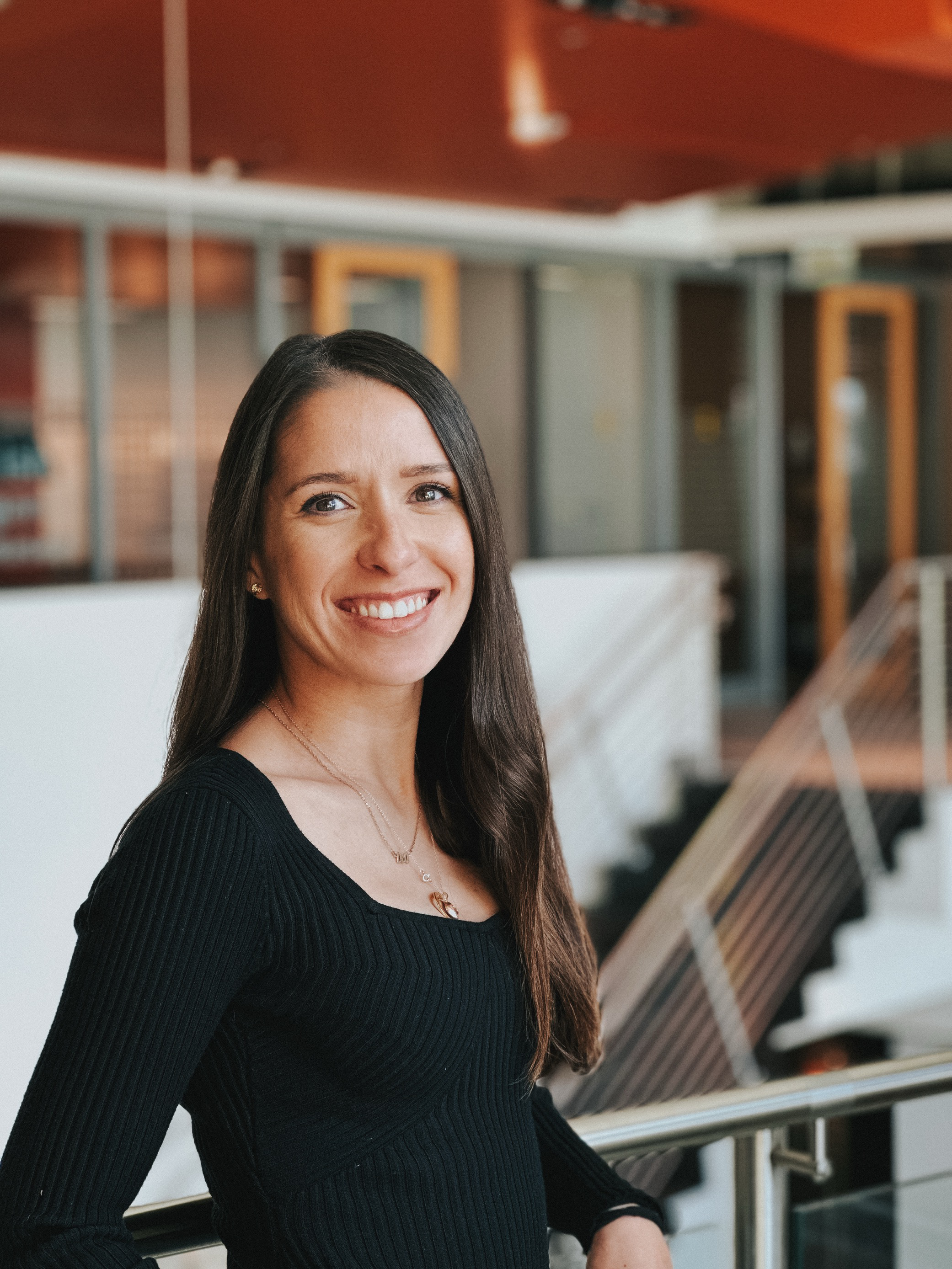 Flower arch with white and red flowers on a brown pot, set up outdoors on green grass with rows of white chairs decorated with flowers and ribbons, against a large wooden fence.
