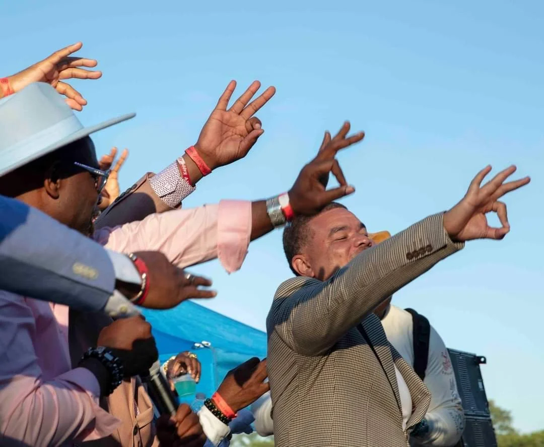 Group of people raising their hands in a celebratory gesture outdoors with a clear blue sky.