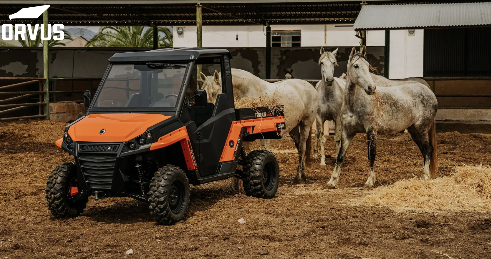 An orange CORVUS UTV and black utility vehicle on a farm with three horses near a barn.