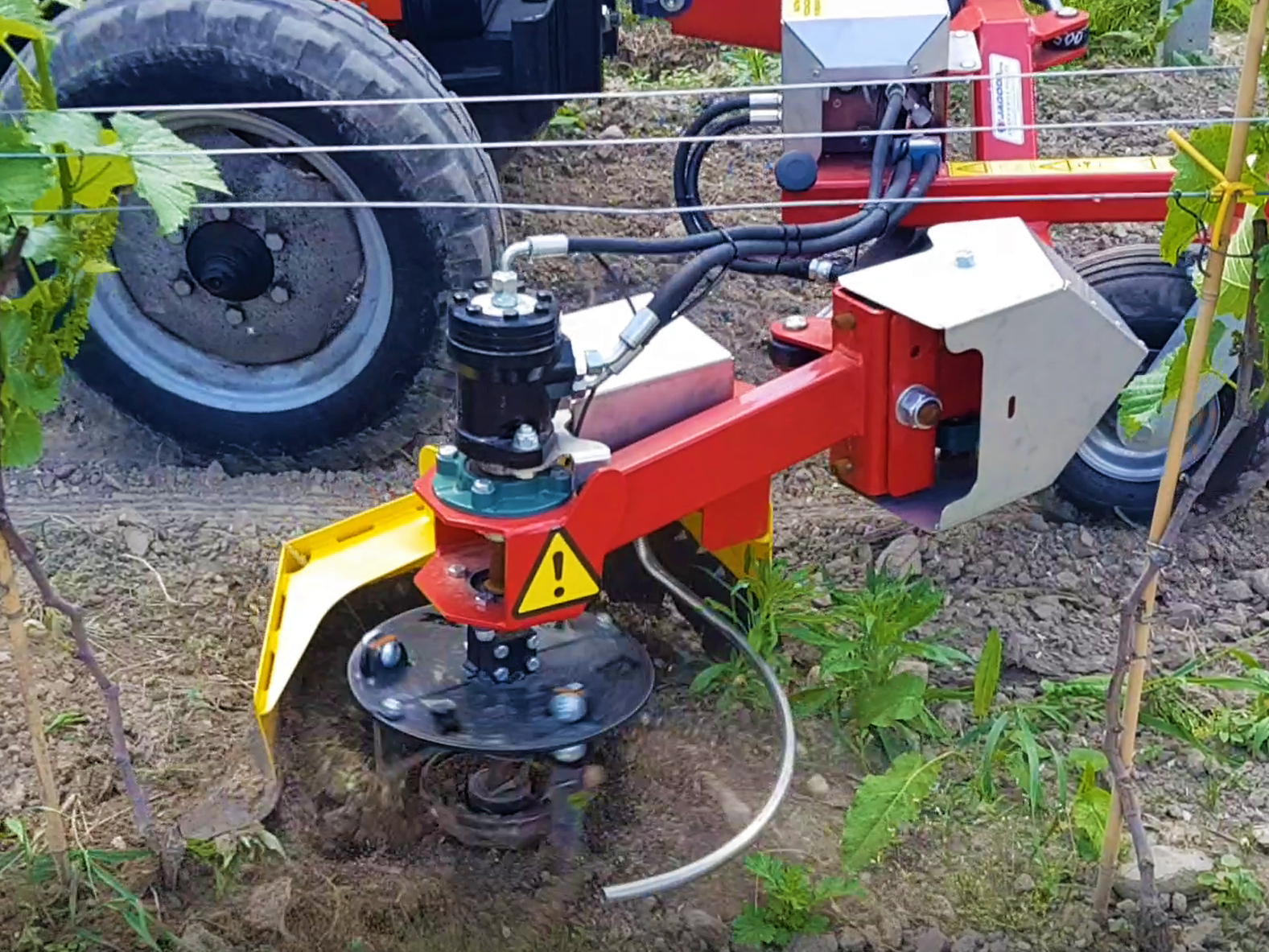 A piece of agricultural machinery in a field, with plants surrounding it and tires in the background. the machinery is the jagoda Lucy