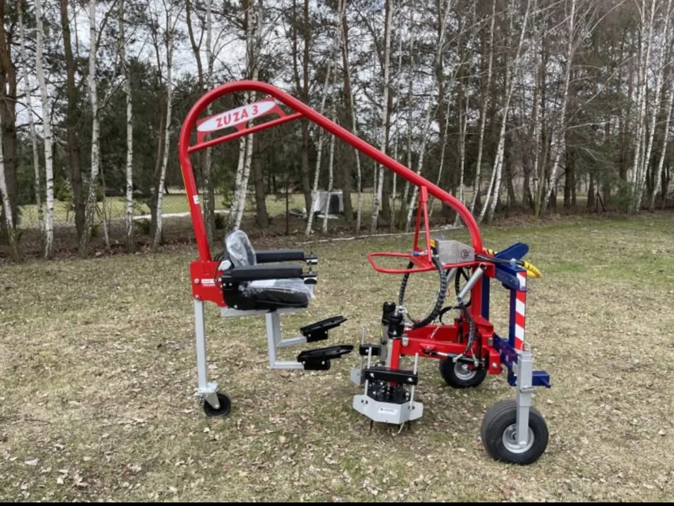 A red, wheeled, motorized rescue chair with black seat and armrests, labeled 'ZUZA 3,' situated outdoors on a grassy area with trees in the background.