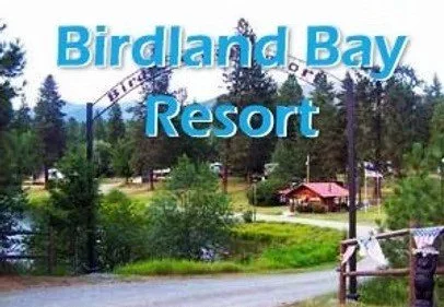Sign for Birdland Bay Resort with trees and greenery in the background.
