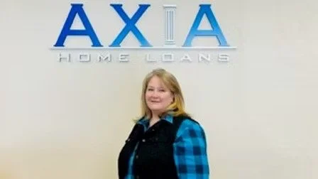 A woman standing in front of a wall with the AXA Home Loans logo.
