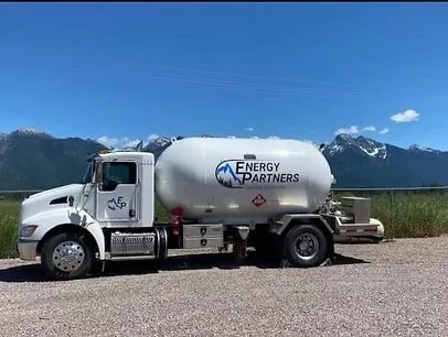 A white Fuel delivery truck with an Energy Partners logo parked on a gravel road with mountains and blue sky in the background.