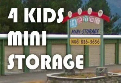 Sign for 4 Kids Mini Storage with phone number, above a storage unit area, with trees and a mountain in the background.