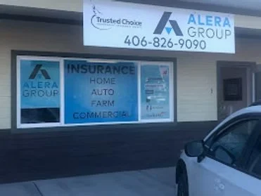 Storefront window with signs for Alera Group and Trusted Choice Insurance, listing services like home, auto, farm, and commercial insurance, and displaying a phone number 406-826-9090.