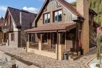 A house with a porch surrounded by other similar houses, paved sidewalk, and trees in the background.