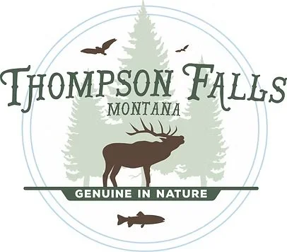 Logo for Thompson Falls, Montana, featuring a moose, pine trees, and flying birds, with the text 'Genuine in Nature'.