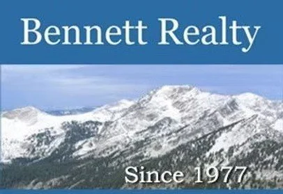 Bennett Realty sign with snowy mountain landscape in the background, and text indicating the company has been in business since 1977.