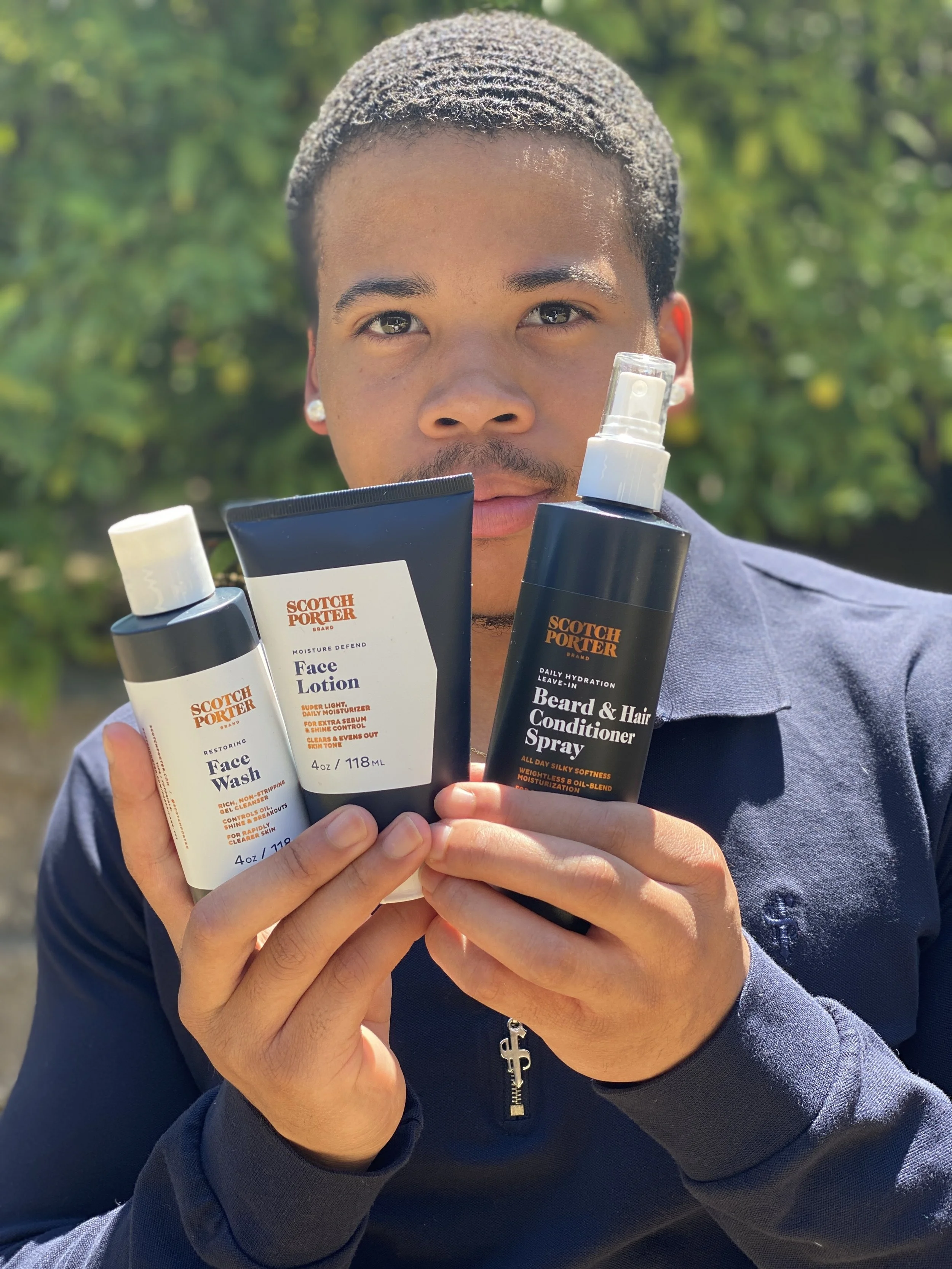 Man holding three skincare products from Scotch Porter, including face wash, face lotion, and beard & hair conditioner spray outdoors.