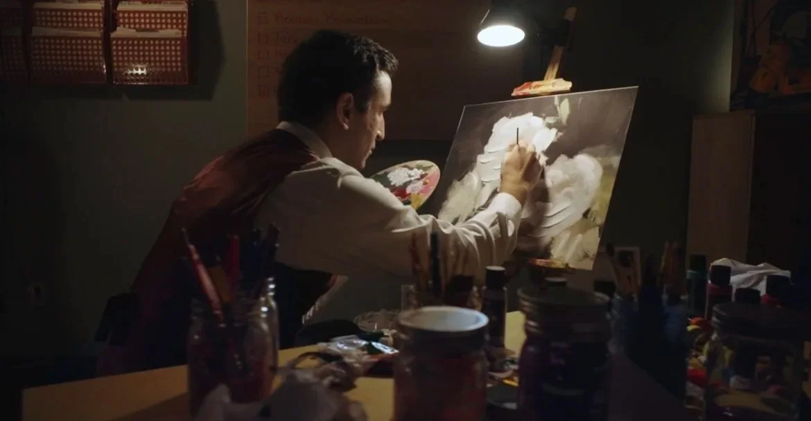Man painting on an easel in a dimly lit room.