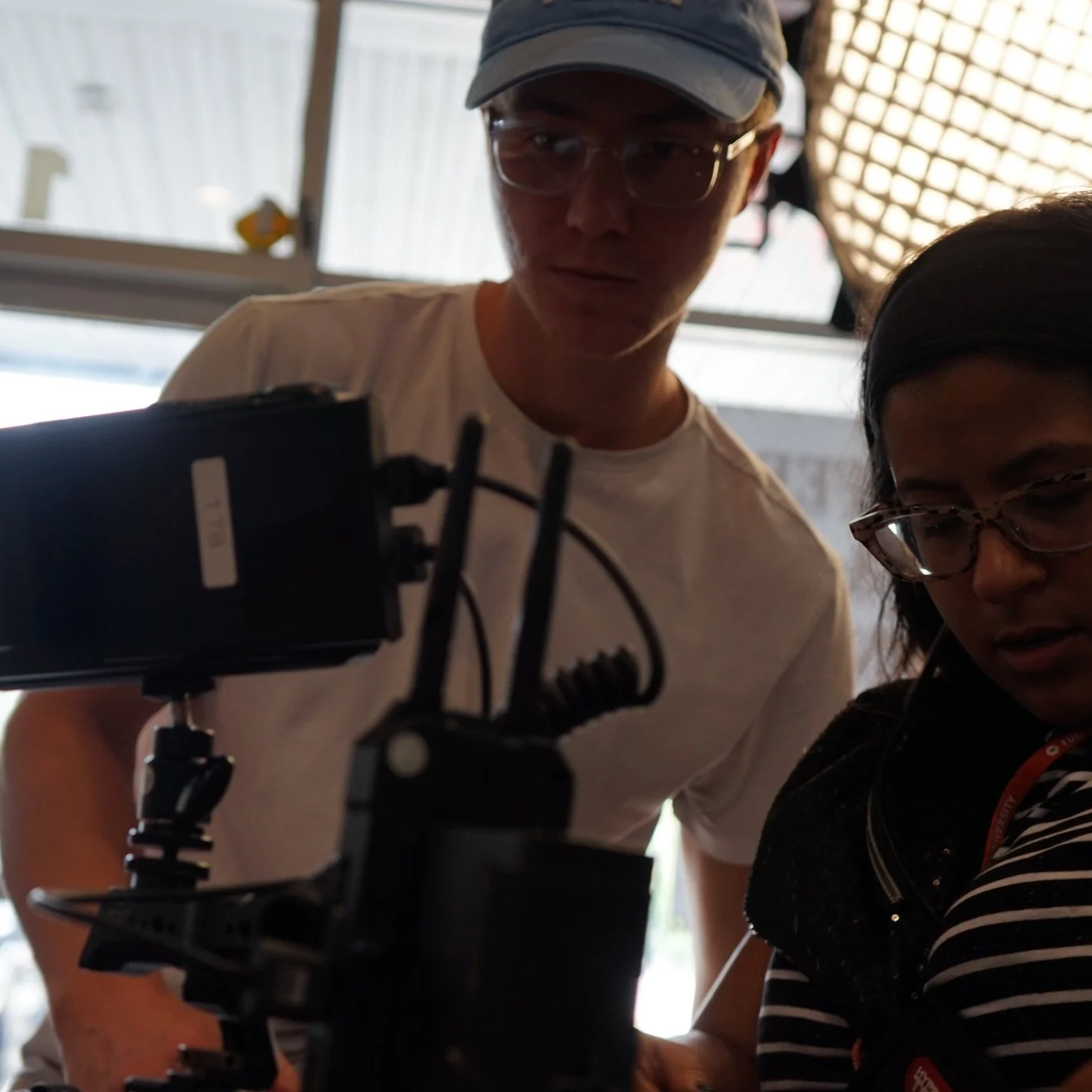 Two people looking at a camera or filming equipment indoors.