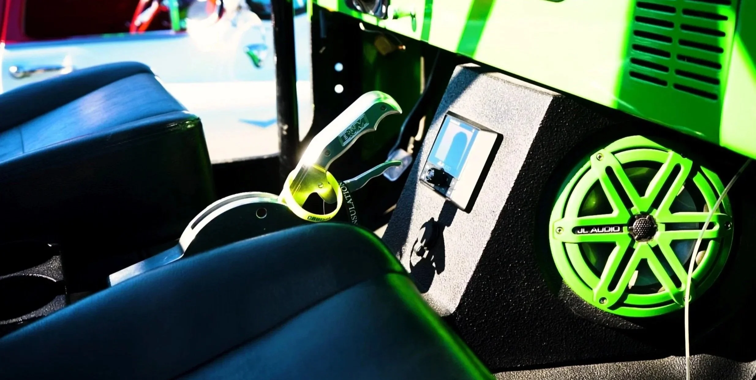 Close-up of a car audio system with a green speaker and control panel, located behind the front seats.