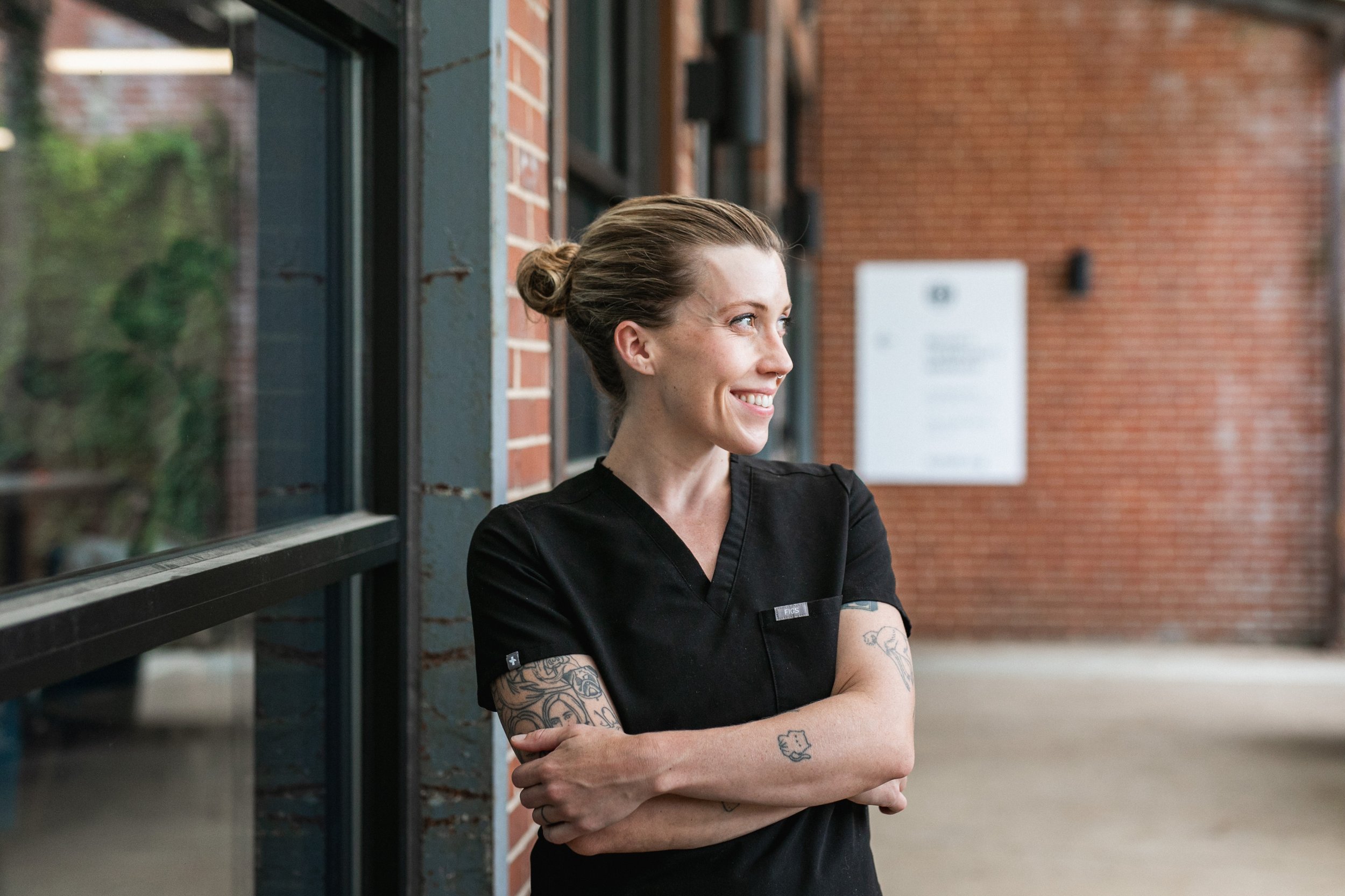 A photo of Clare wearing scrubs and smiling. She is looking to her left with her arms crossed.