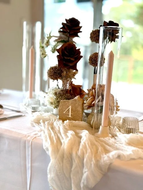 Table centerpiece with tall glass vases, roses, and candles, with a table number '4' card.