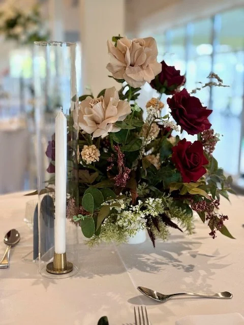 Elegant floral centerpiece with roses and greenery, and a tall candle holder with a white candle on a decorated dining table.