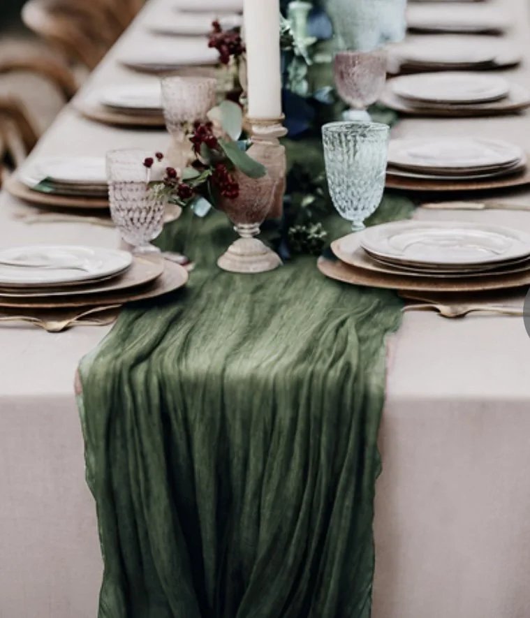 A dining table decorated with a green table runner, plates, crystal glasses, candles, and floral accents for an elegant meal setting.