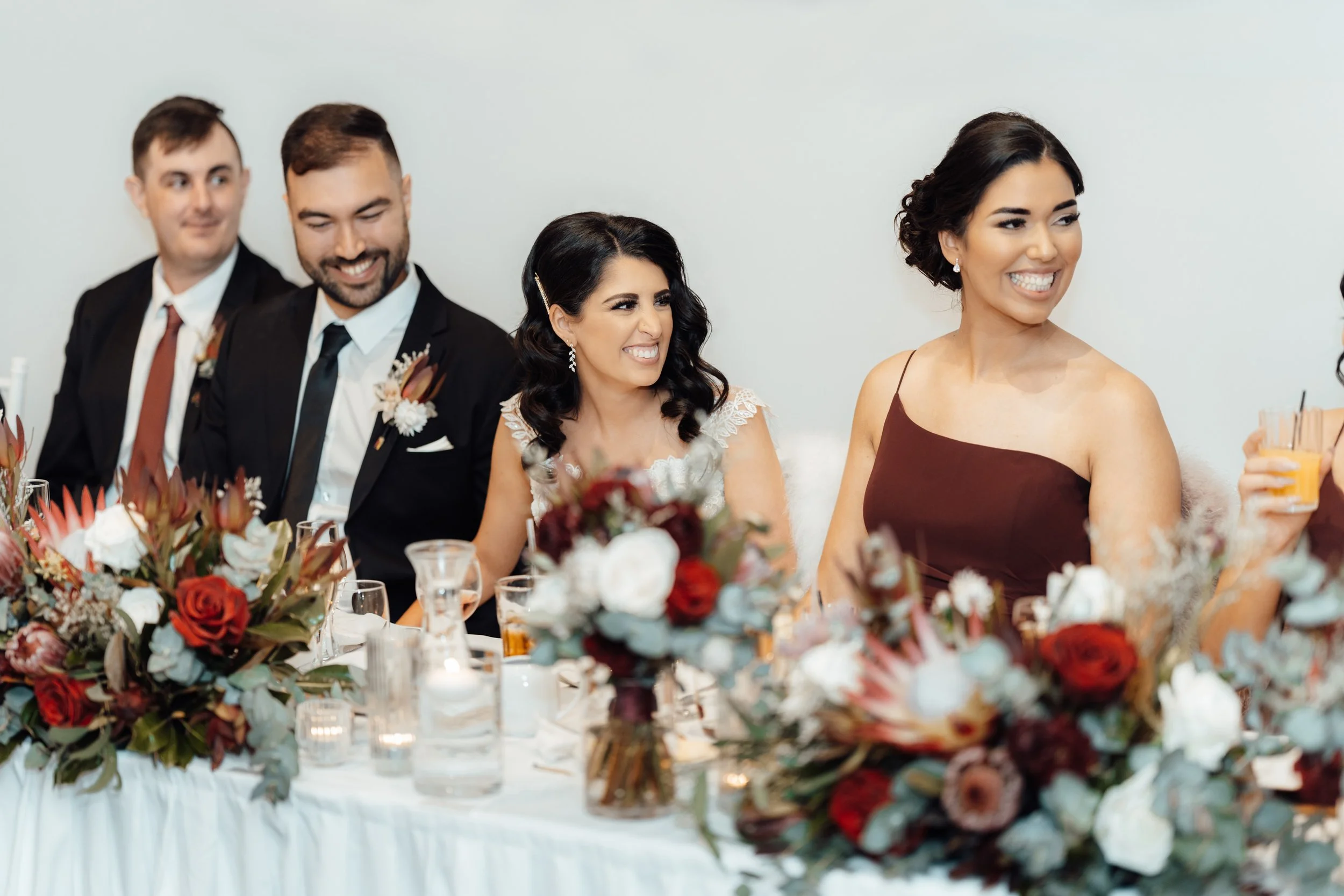 People sitting at a decorated wedding reception table with floral arrangements and candles, smiling and enjoying the celebration.