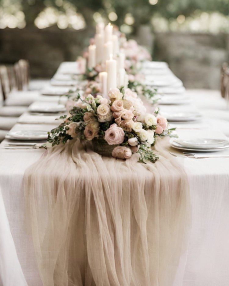 Elegant outdoor dining table decorated with a soft pink tulle table runner, floral centerpiece with pink and white roses and candles.
