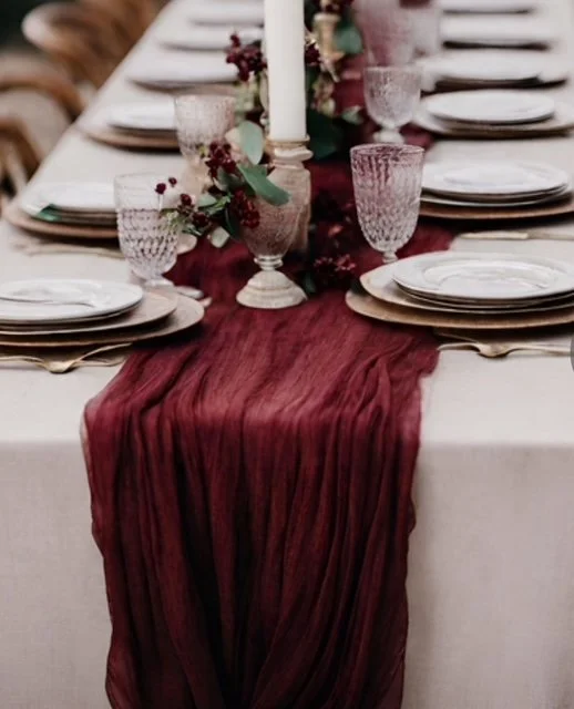 Elegant dinner table with a burgundy table runner, glassware, plates, and floral centerpieces.