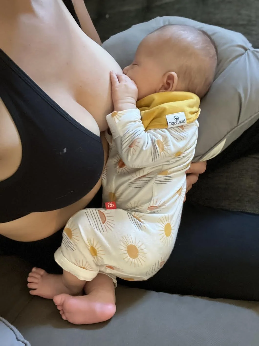 A baby nursing while lying on a woman's chest, with the woman sitting on a couch.