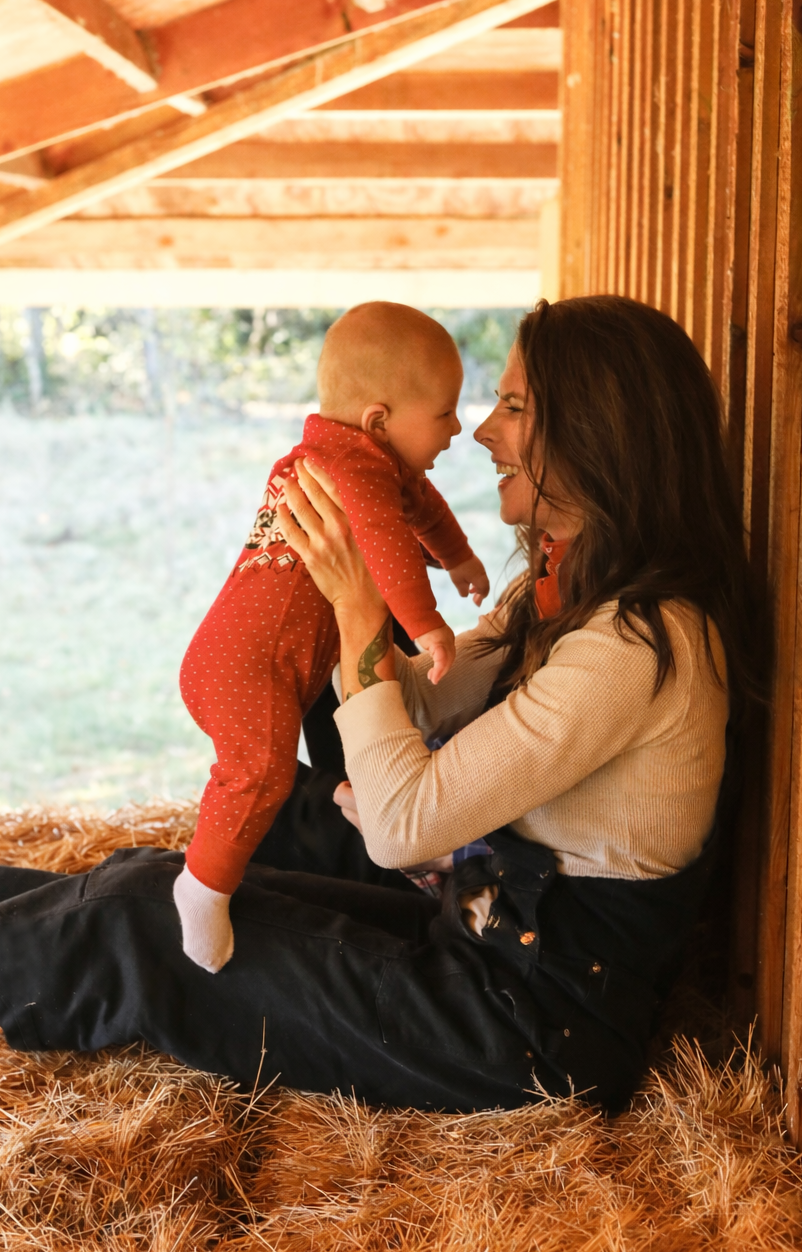 A woman and a young child sharing a joyful moment inside a wooden structure with straw on the ground. They are holding each other and smiling at each other.