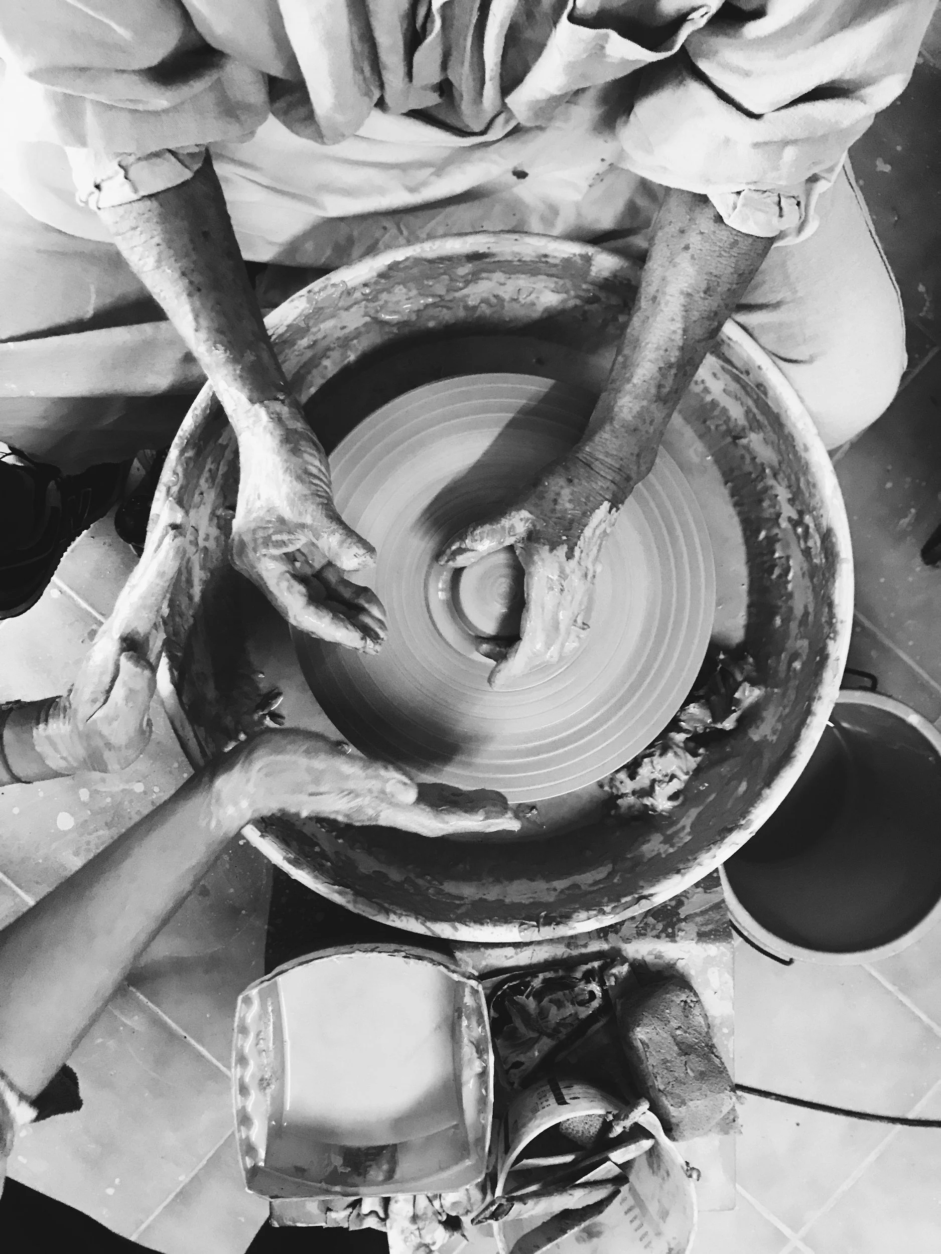 Two people shaping pottery on a spinning wheel in a pottery studio.